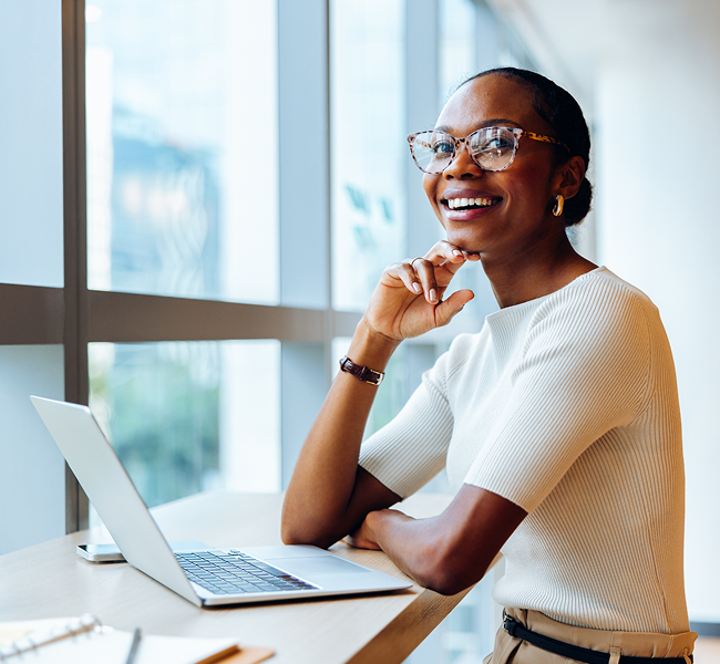 Smiling woman in glasses and a white top working at a laptop in a bright office