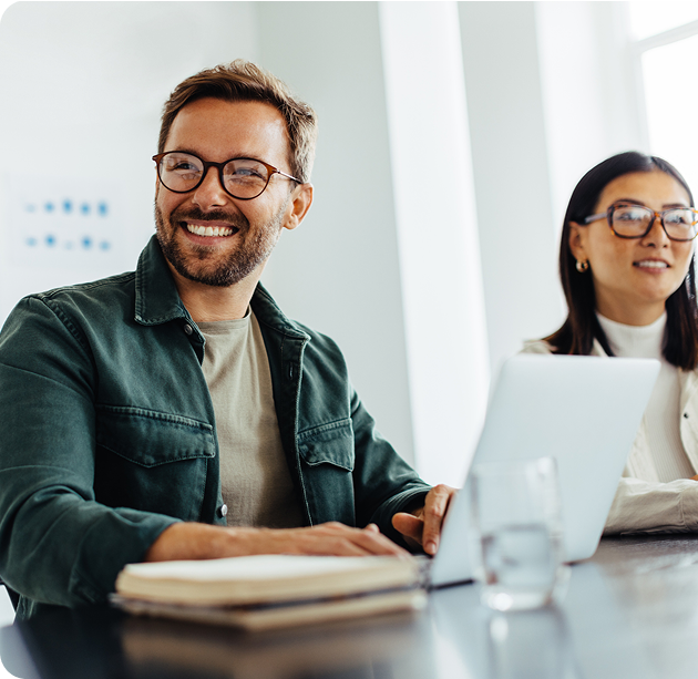 Man in a denim shirt and woman in glasses collaborating at a laptop